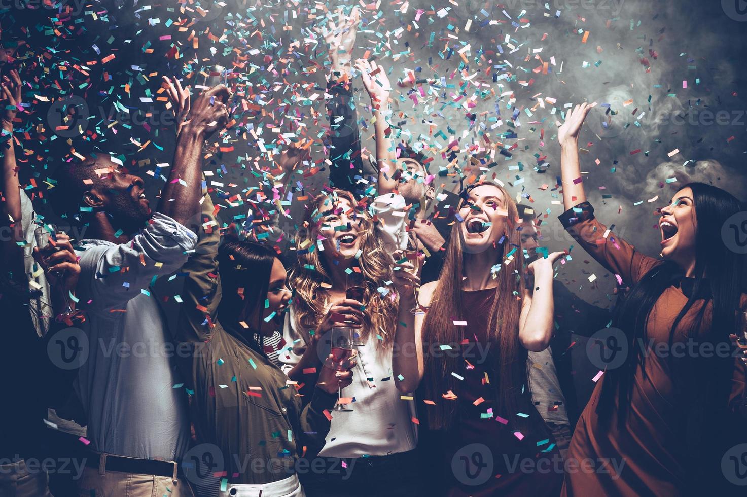 Unleashed fun. Group of beautiful young people throwing colorful confetti while dancing and looking happy photo