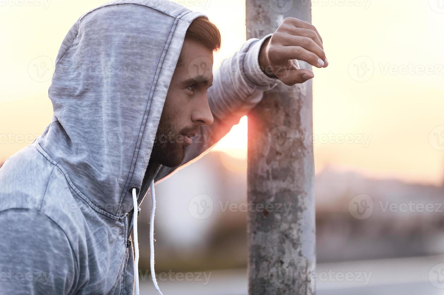 Taking a minute break. Side view of thoughtful young man wearing hood and looking away while standing outdoors photo