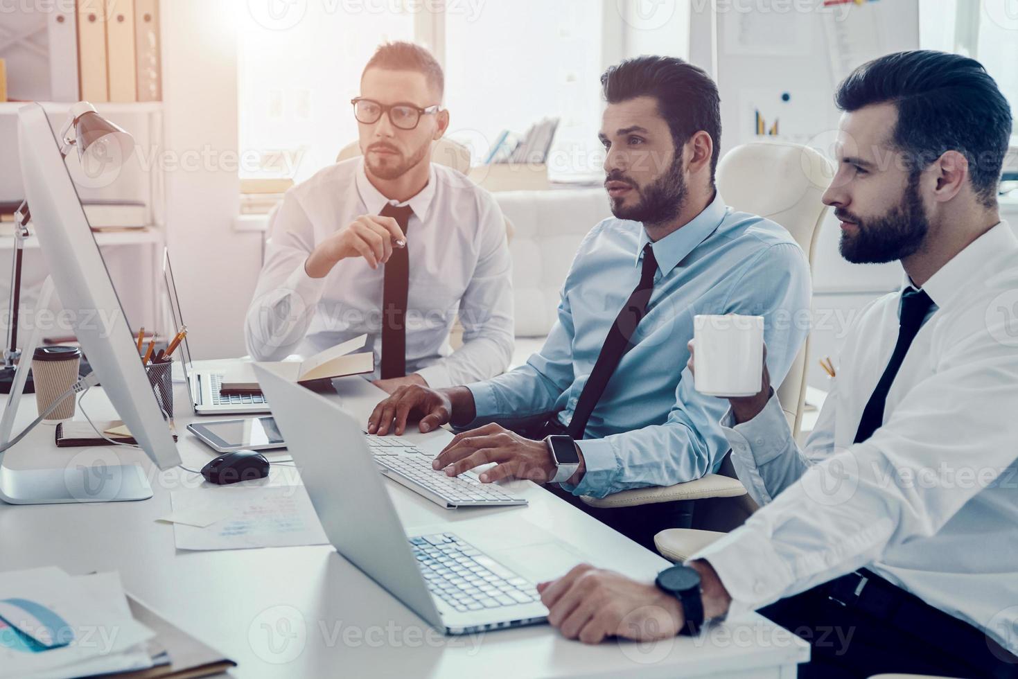 Young business professionals. Group of young modern men in formalwear working using computers while sitting in the office photo