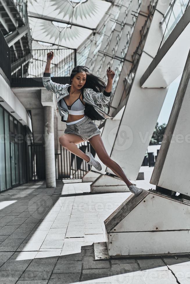 ella está llena de energía. toda una mujer joven y atractiva con ropa informal mirando hacia otro lado y gesticulando mientras salta al aire libre foto