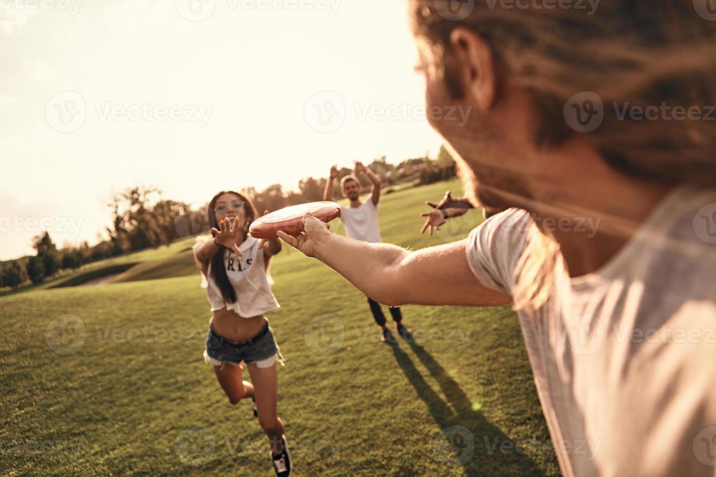 Group of young people in casual wear playing frisbee while spending carefree time outdoors photo