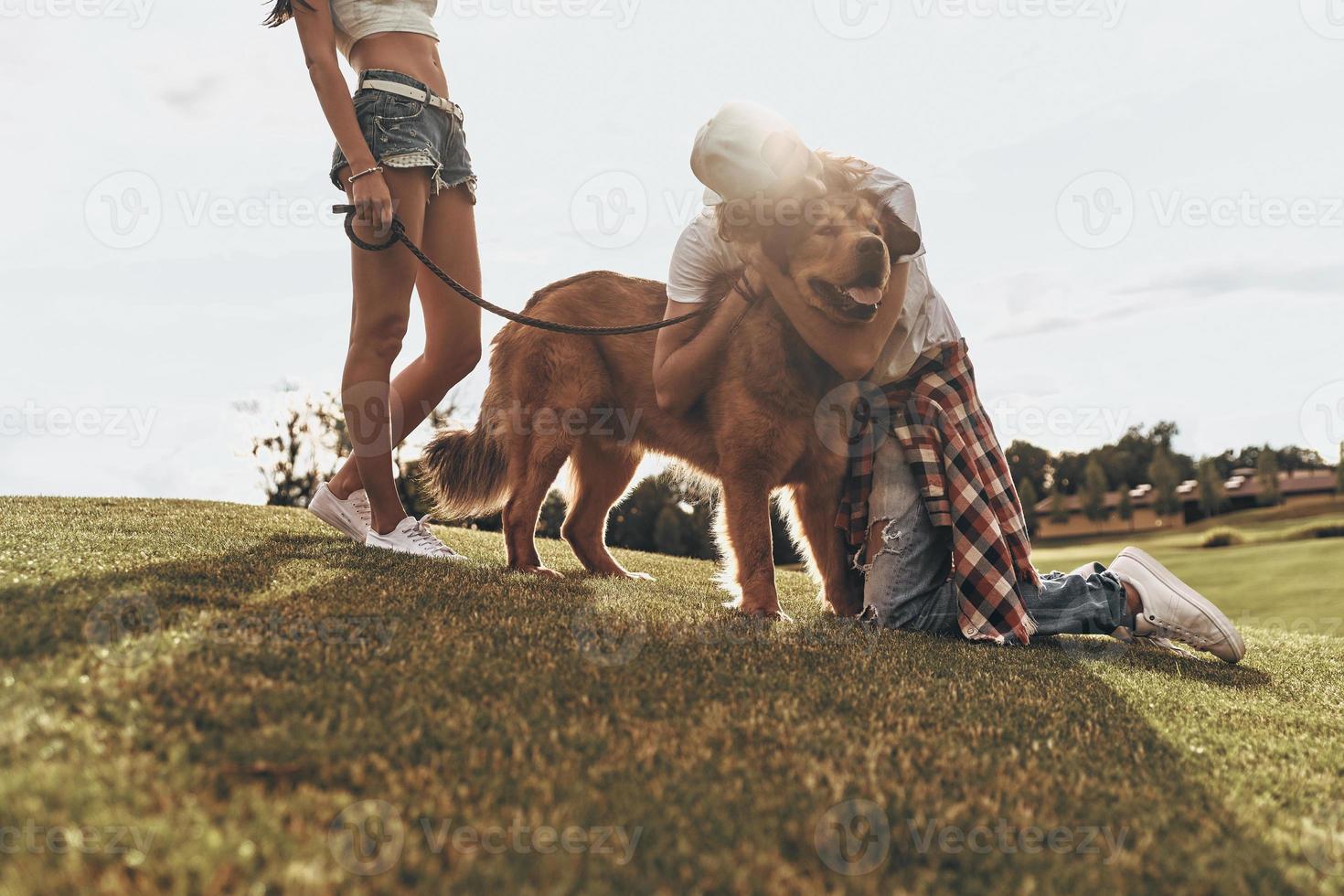 Expressing true love. Handsome young man embracing his dog while spending free time with his girlfriend in the park photo