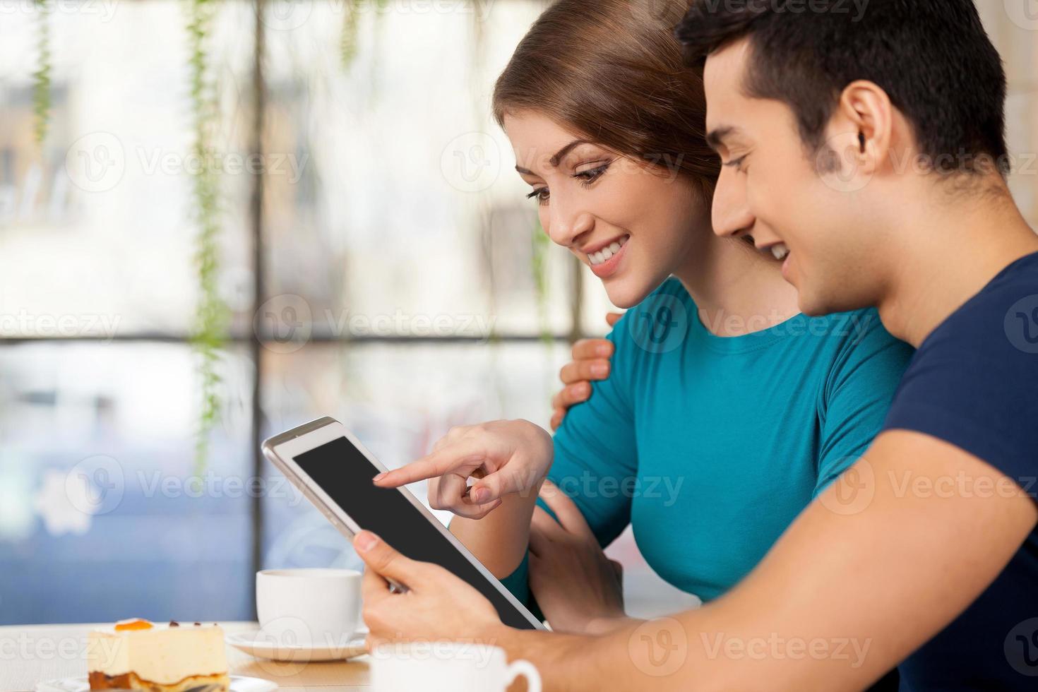 Couple with digital tablet. Side view of cheerful young loving couple sitting at the restaurant and using digital tablet photo