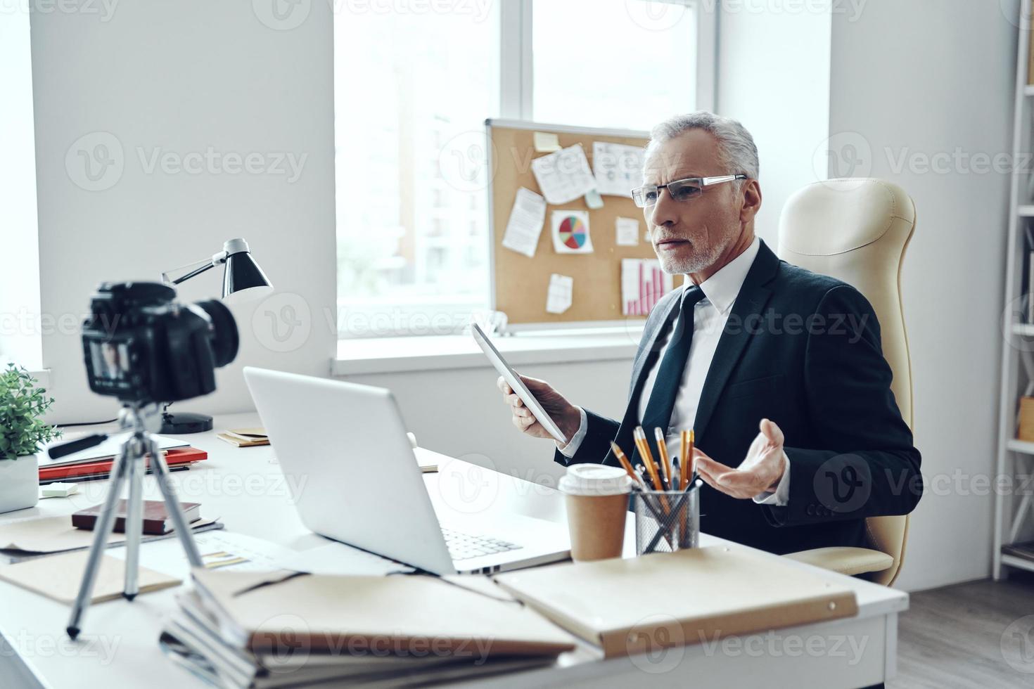 Senior man in elegant business suit using modern technologies while making social media video photo