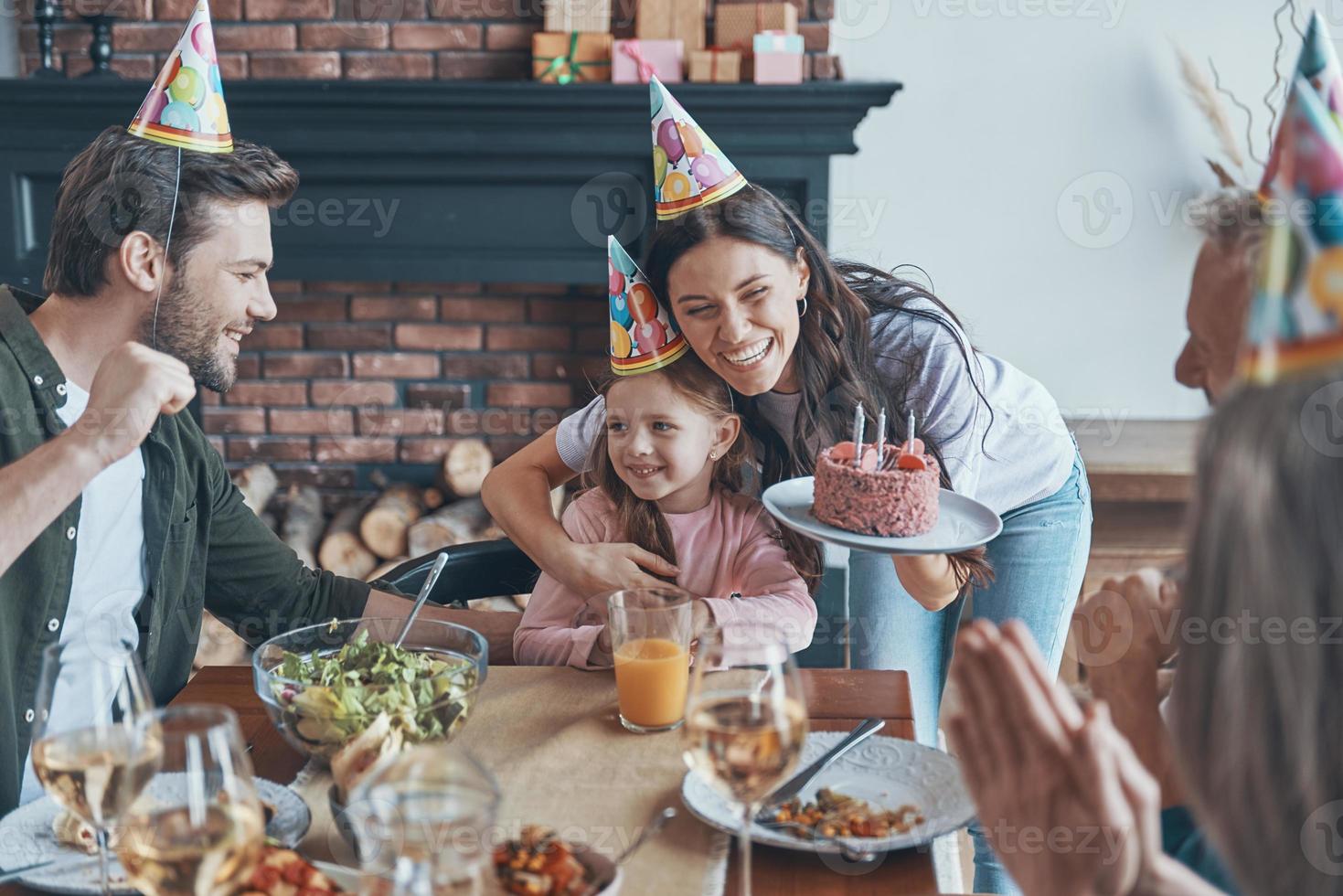 Happy family celebrating birthday of little girl while sitting at the dining table at home photo