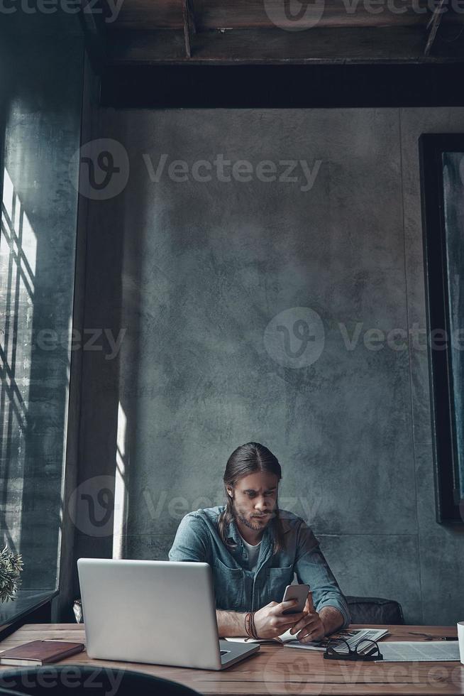 respondiendo mensajes importantes. un joven serio que usa su teléfono inteligente mientras está sentado en el escritorio de la oficina foto