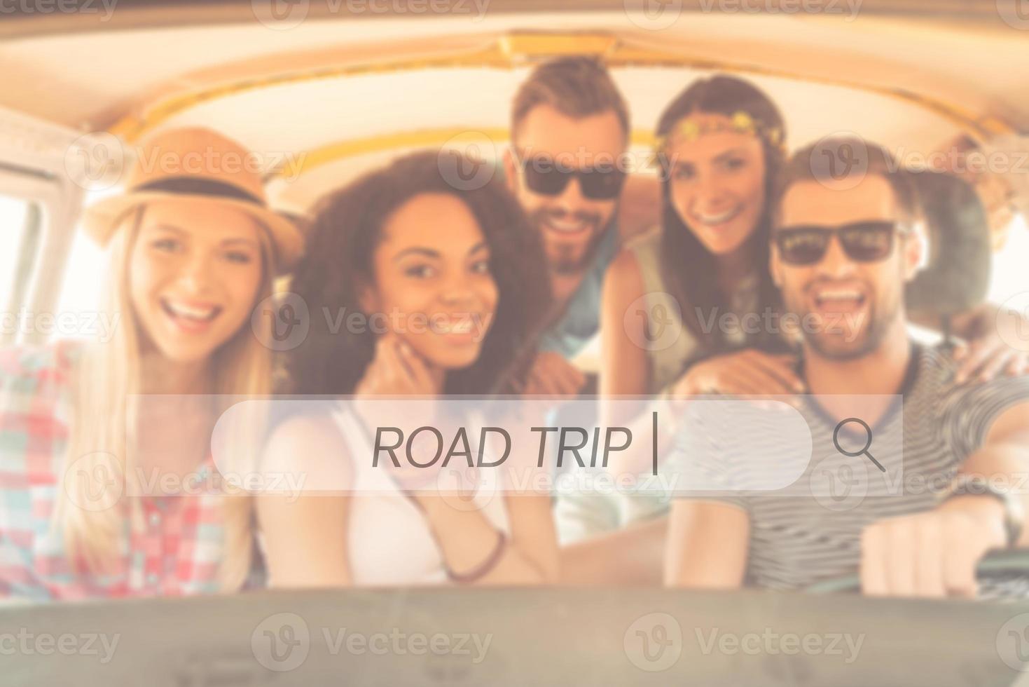 Road trip. Group of joyful young people smiling at camera while sitting inside of minivan together photo