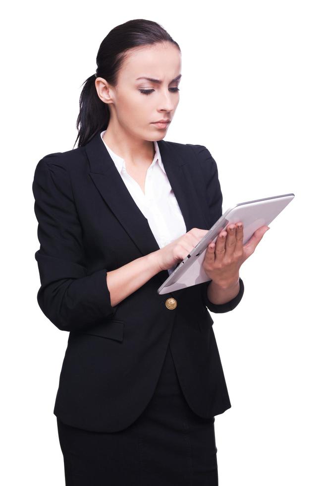 Working on digital tablet. Confident young woman in formalwear working on digital tablet and smiling while standing isolated on white photo