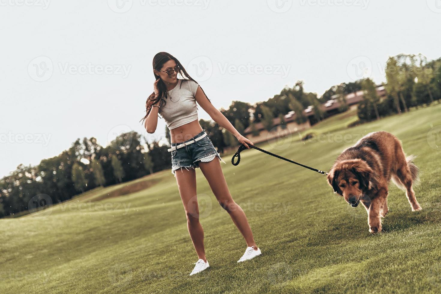 Summer filled with joy. Full length of beautiful young woman playing with her dog and smiling while standing outdoors photo