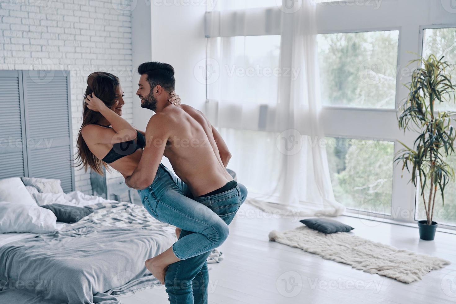 No rules for them. Handsome young shirtless man carrying semi-dressed attractive woman while standing in the bedroom photo