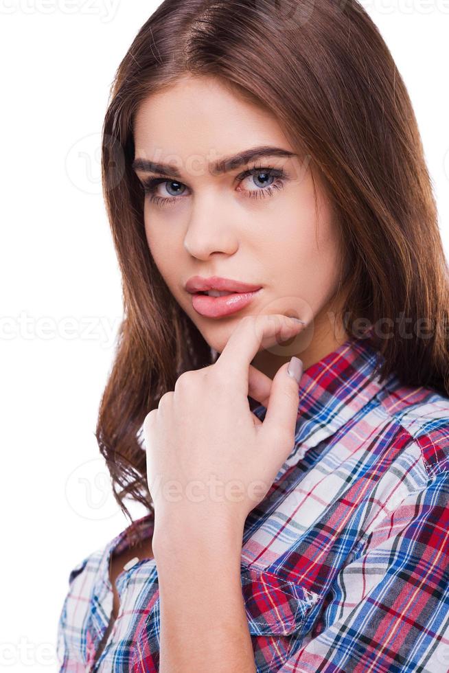 Thoughtful beauty. Beautiful young woman in shirt holding hand on chin and looking at camera while standing against white background photo