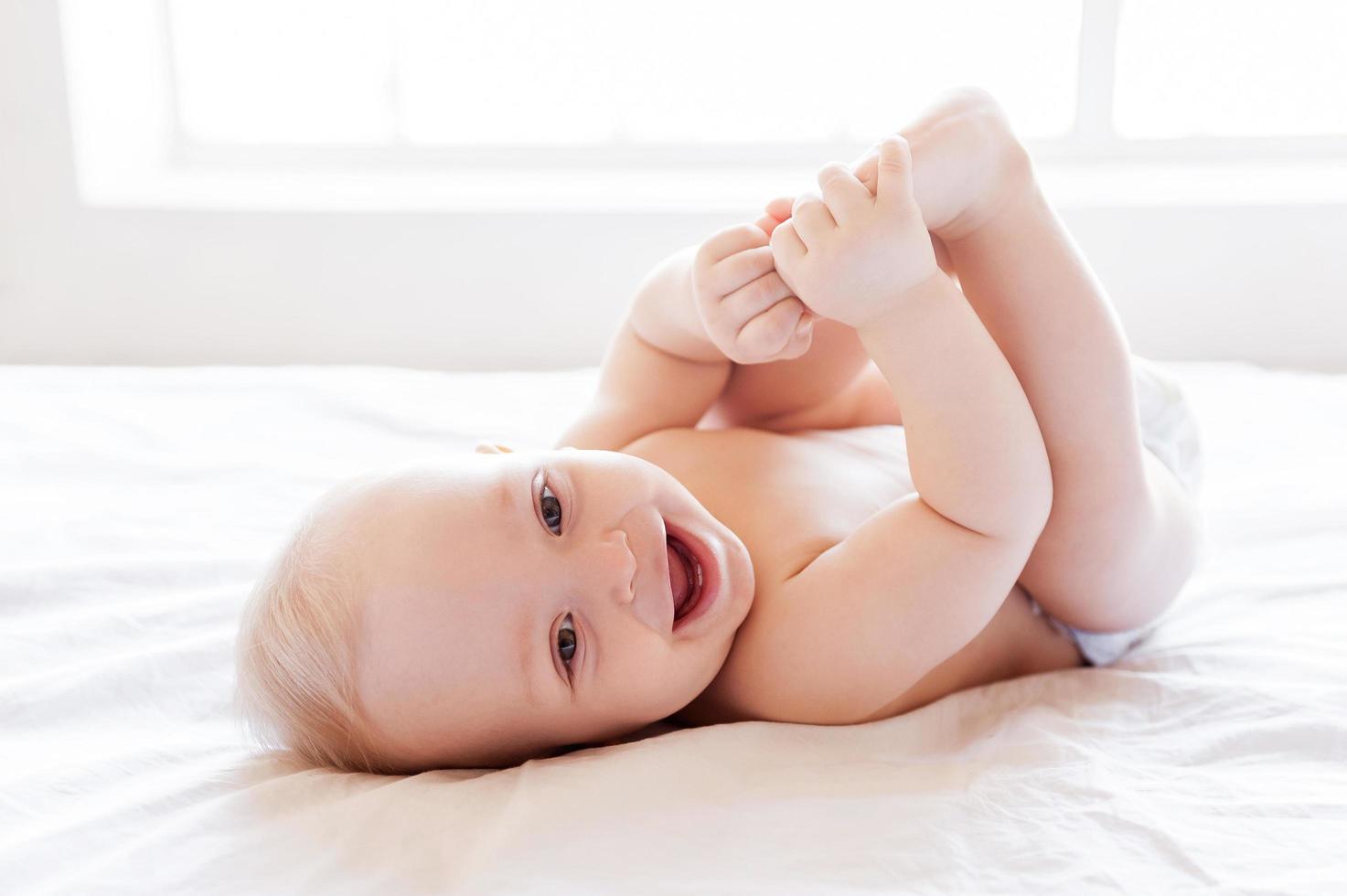 sentirse seco y feliz. pequeño bebé feliz sonriendo mientras está acostado en la cama foto