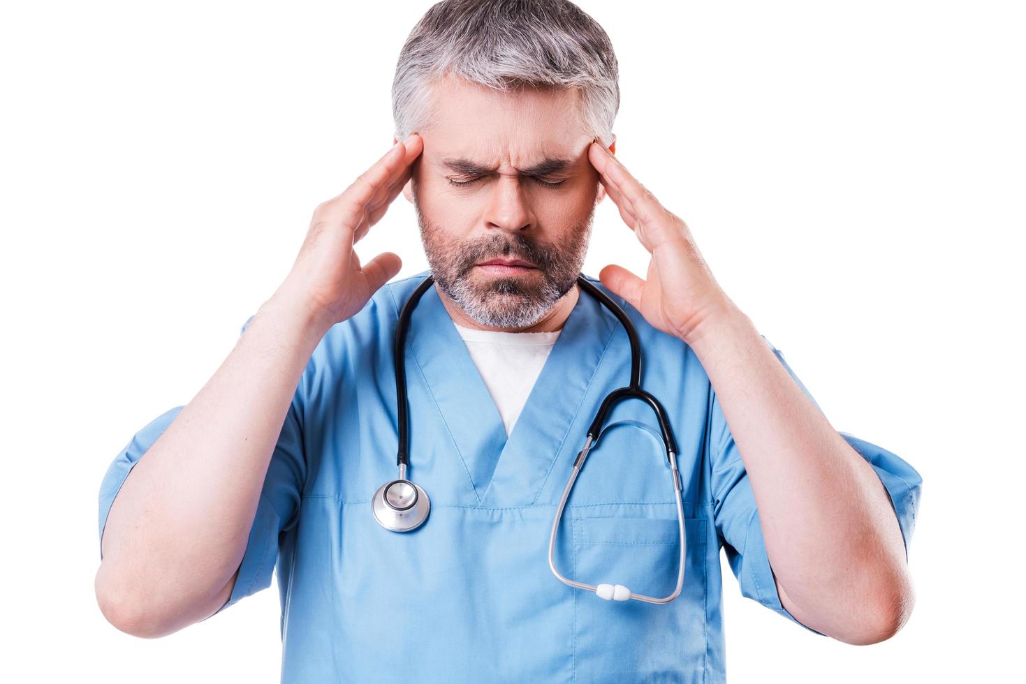 Stressed surgeon. Depressed mature surgeon touching his head with hands and keeping eyes closed while standing isolated on white photo