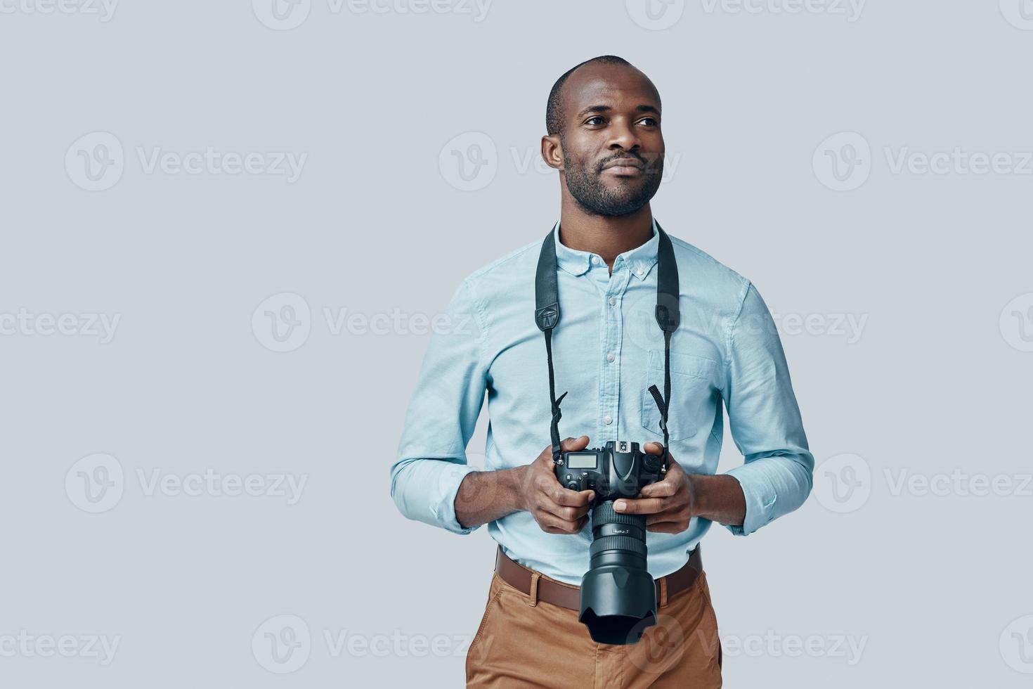 Handsome young African man looking away and smiling while standing against grey background photo