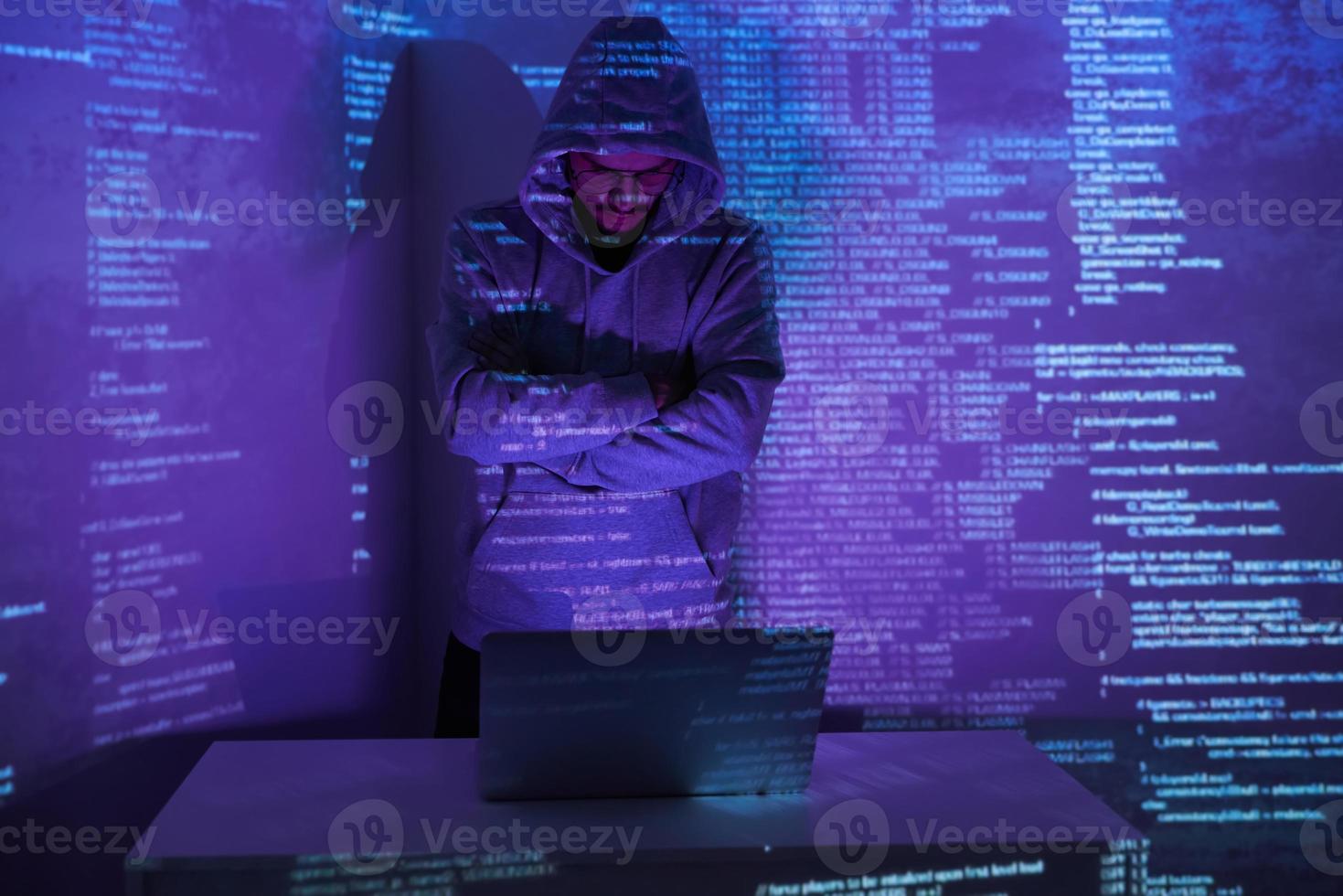 Young man in hooded shirt using computer against dark background photo