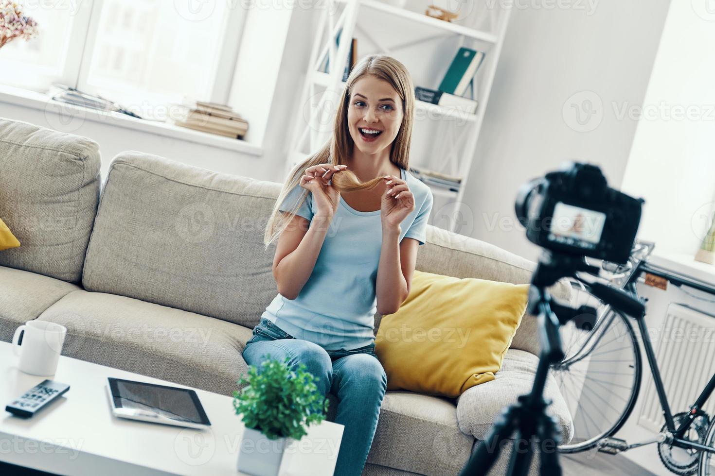 hermosa joven sonriendo y mostrando sus puntas de cabello mientras hace videos en las redes sociales en casa foto