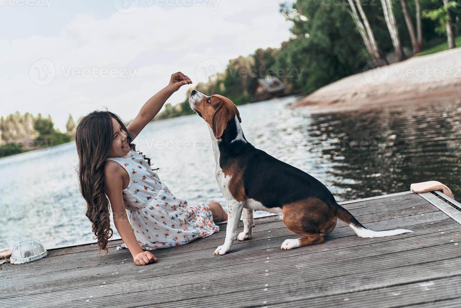 Playing with pet. Cute little girl playing with her dog while sitting near the lake outdoors photo