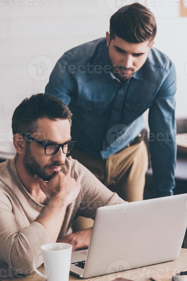 He needs an expert advice. Thoughtful men looking at laptop while sitting at the office table on business meeting with their coworkers photo