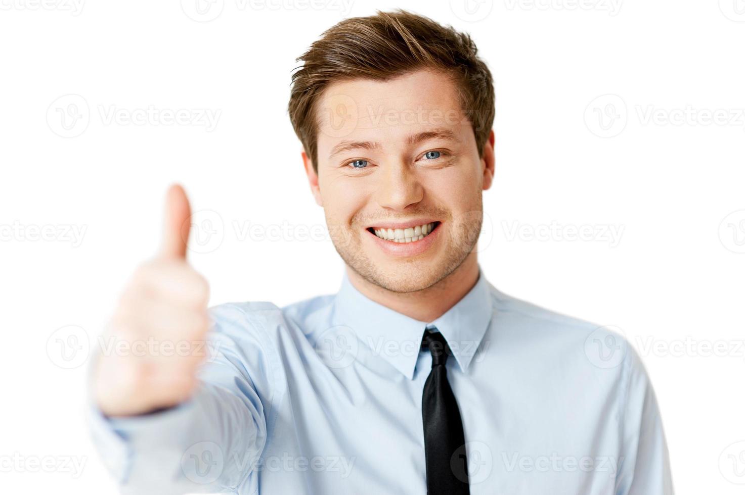 todo es genial hombre joven guapo con camisa y corbata mostrando su pulgar hacia arriba y sonriendo mientras está de pie aislado en blanco foto