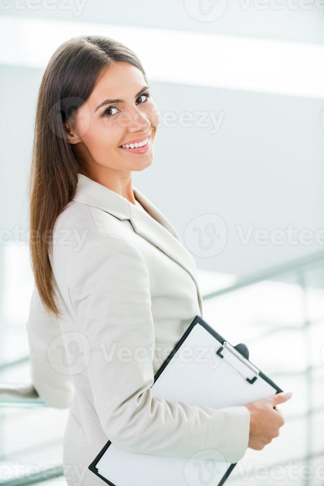 Young and successful businesswoman. Rear view of beautiful young smiling businesswoman in formalwear walking by staircase and looking over shoulder photo