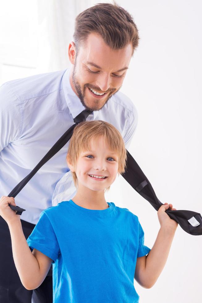Playful father and son. Playful little boy stretching necktie of his father standing near him and smiling photo