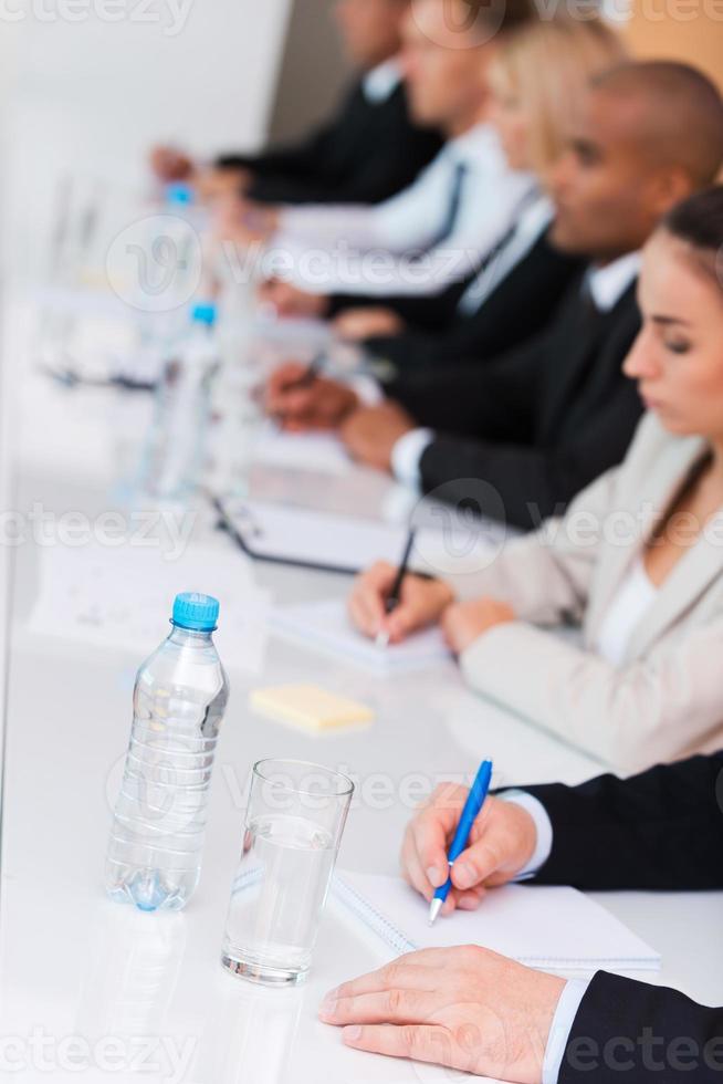 Business conference. Side view of business people writing something in their note pads while sitting in a row photo