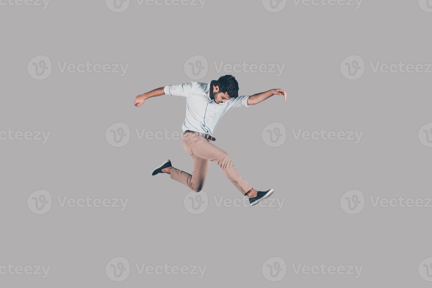 Man jumping. Mid-air shot of handsome young man jumping and gesturing against background photo