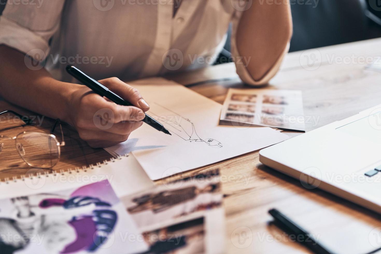 Working on trending designs. Close up of young woman working on sketches while sitting in her workshop photo
