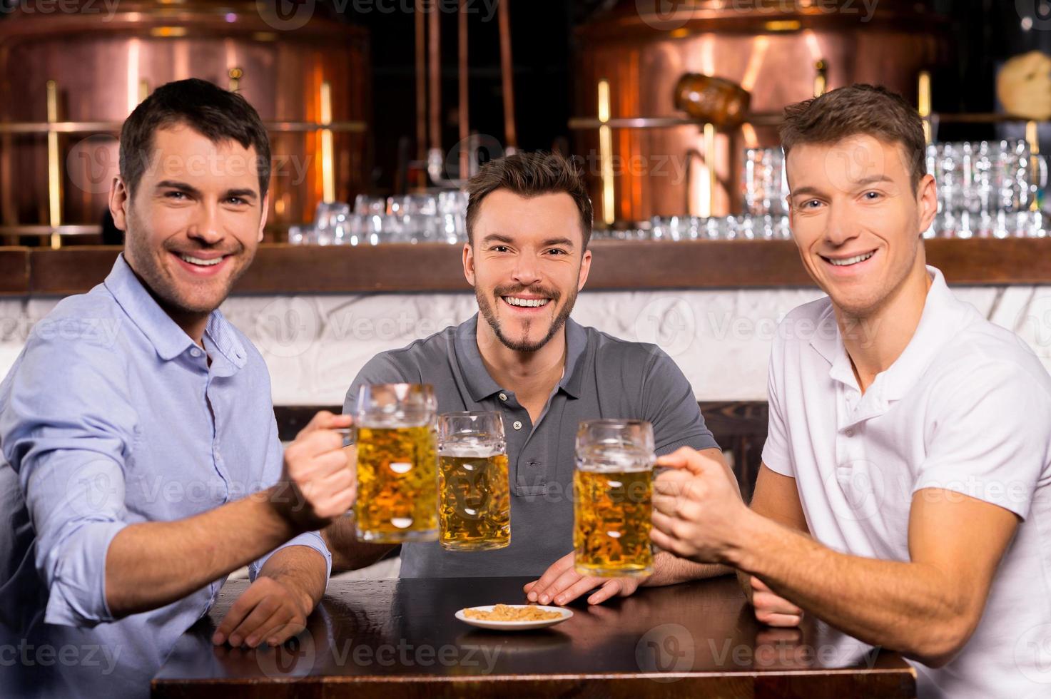 Having a good time. Three cheerful friends holding mugs with lager and smiling at camera photo
