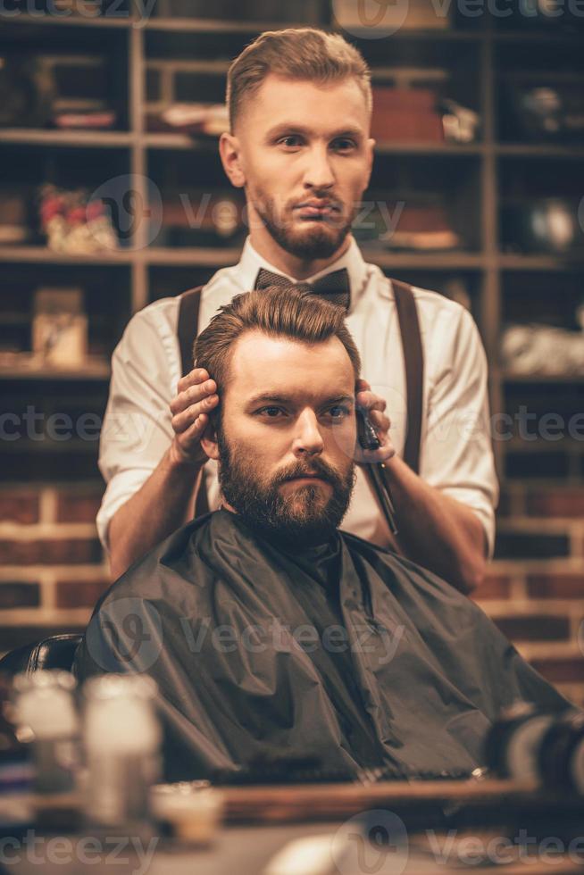 Checking symmetry. Hairdresser checking symmetry of haircut of his client at barbershop photo