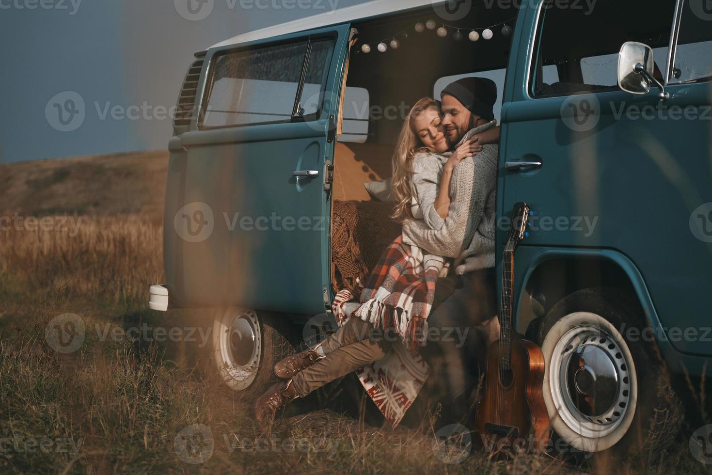 Feeling warm in his arms.  Handsome young man embracing his beautiful girlfriend and smiling while sitting in blue retro style mini van photo