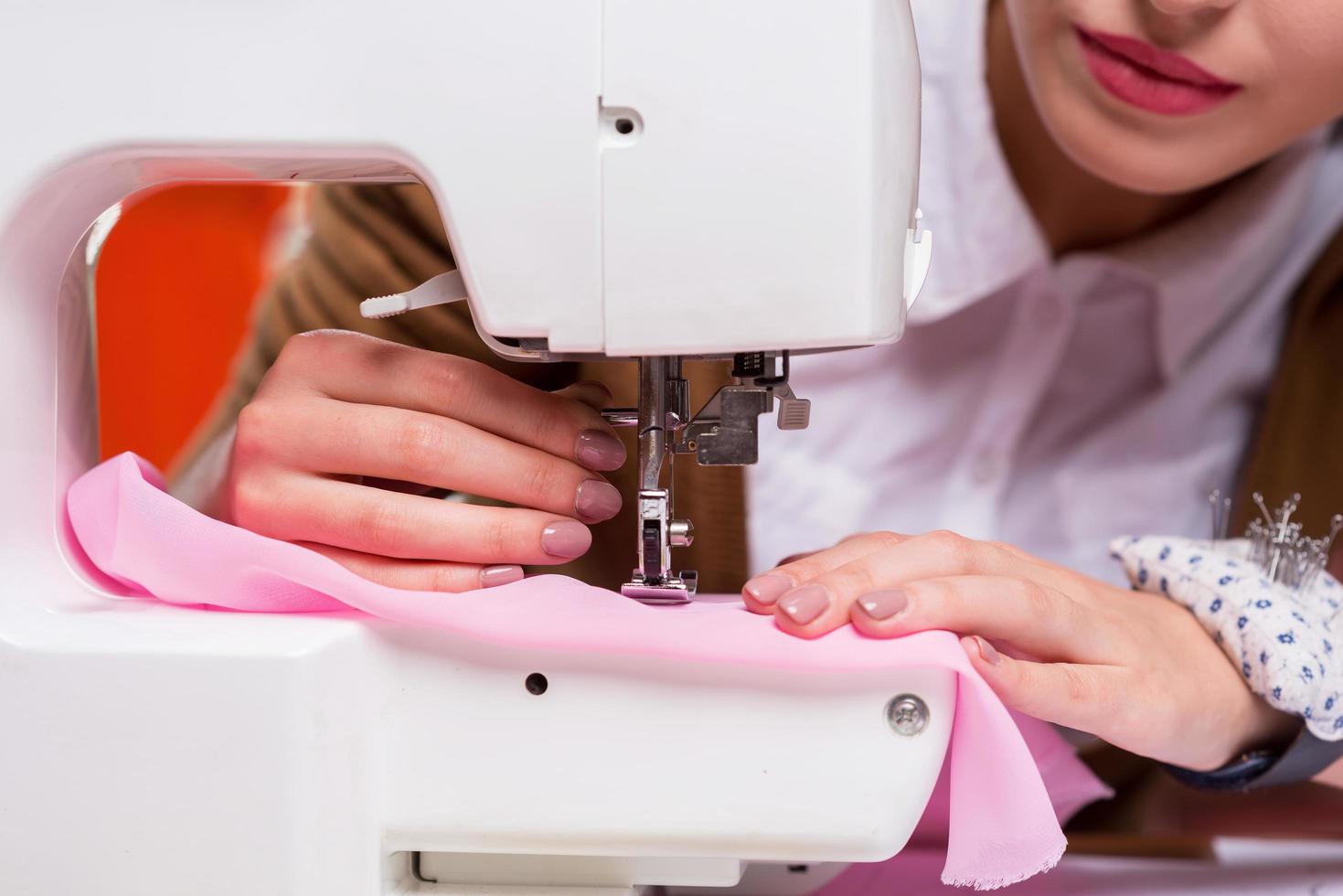 Fashion designer at work. Close-up of female fashion designer working on sewing machine while sitting at her working place photo