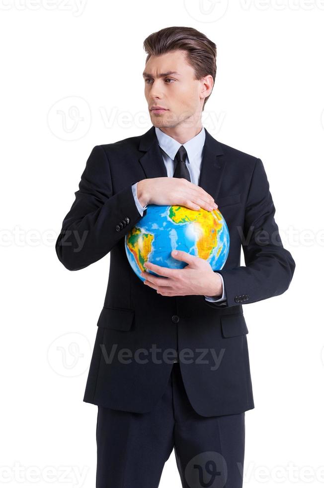 World in his hands. Confident young man in formalwear holding globe and looking away while standing isolated on white photo