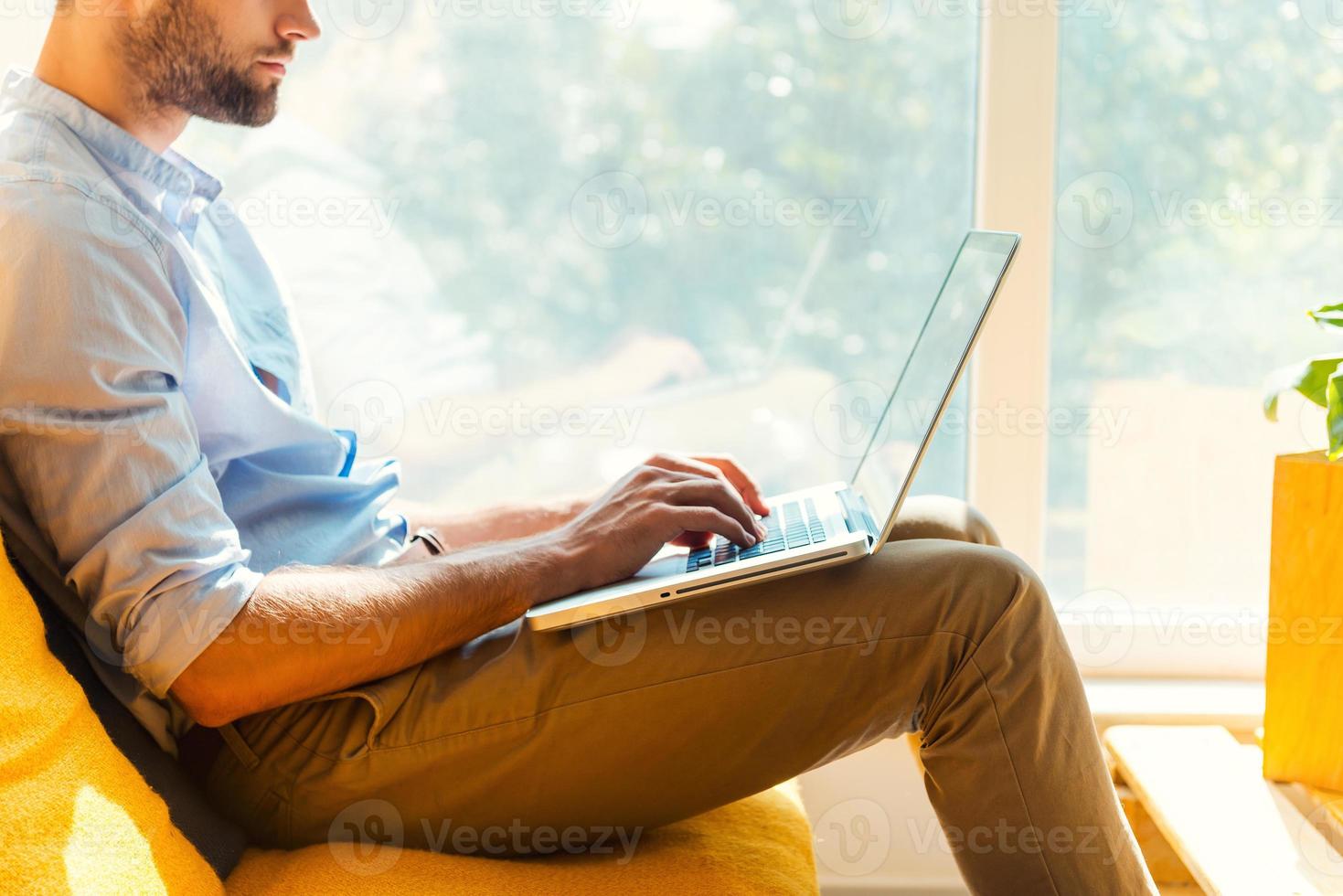 Focused on his work. Close-up of young man working on laptop while sitting in the rest area of the office photo