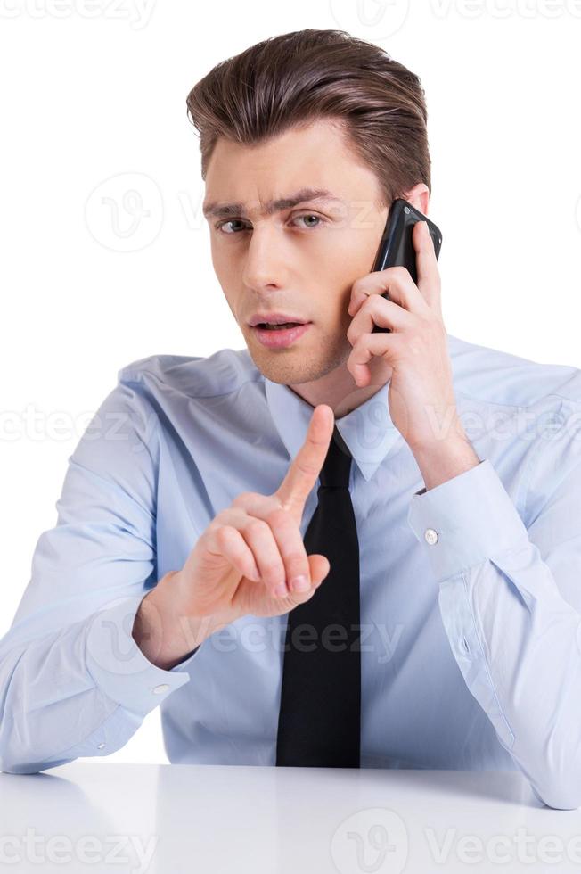 Cheerful interviewer. Handsome young man in shirt and tie sitting at the table and gesturing while isolated on white photo