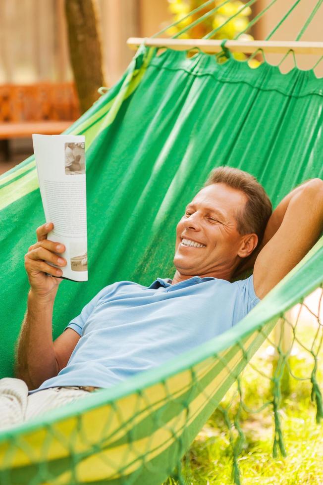 tiempo para relajarse. hombre maduro feliz acostado en una hamaca y leyendo una revista foto