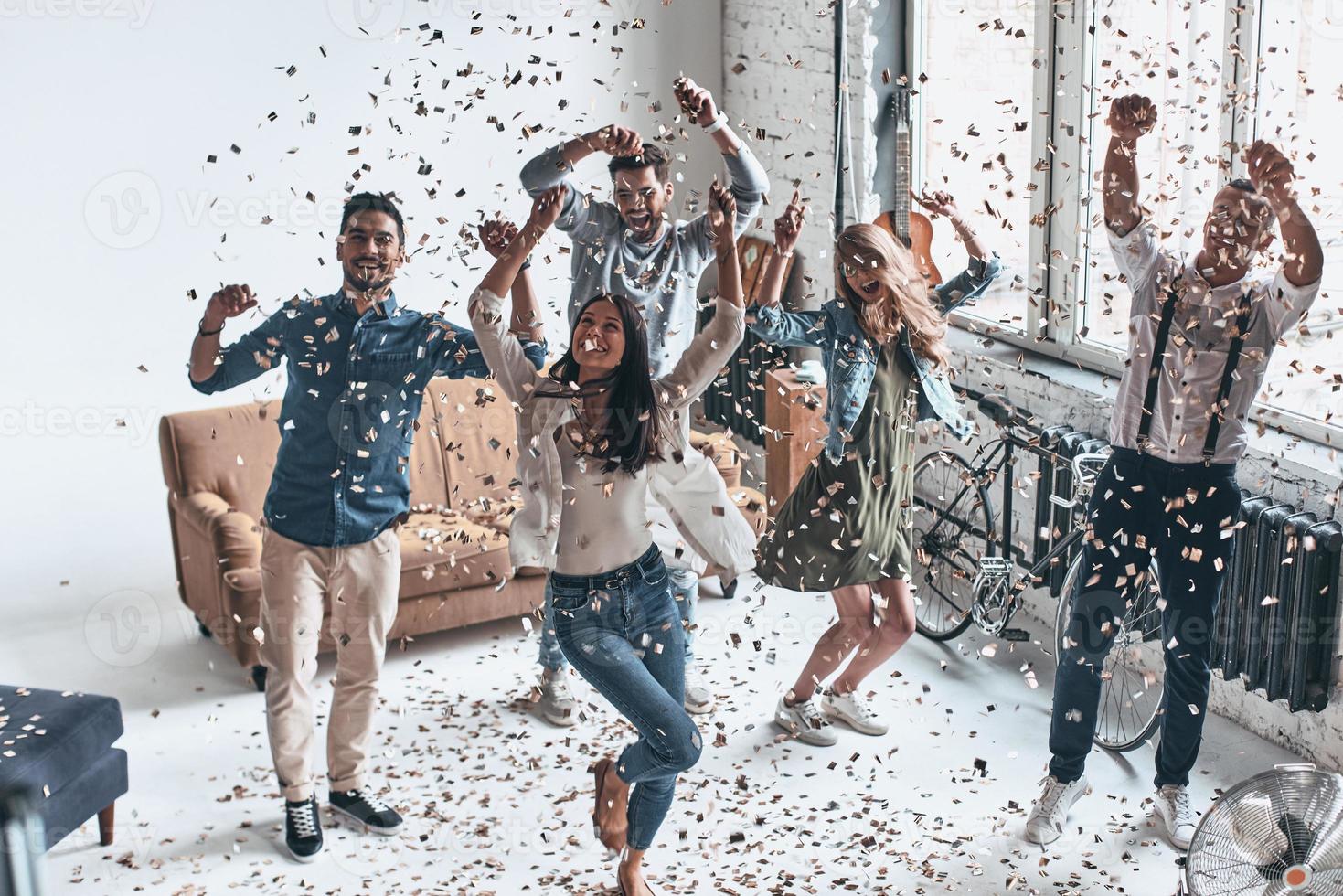 simplemente sintiéndome feliz. vista superior completa de jóvenes felices gesticulando y sonriendo mientras bailan con confeti volando por todas partes foto