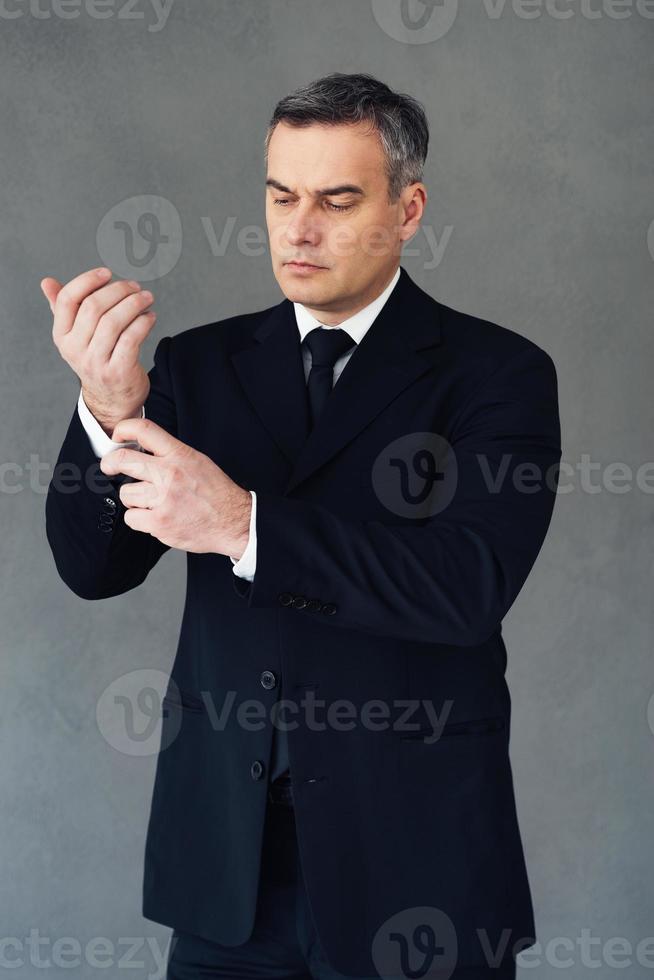 Confident till last button. Mature businessman adjusting his shirtsleeve while standing against grey background photo