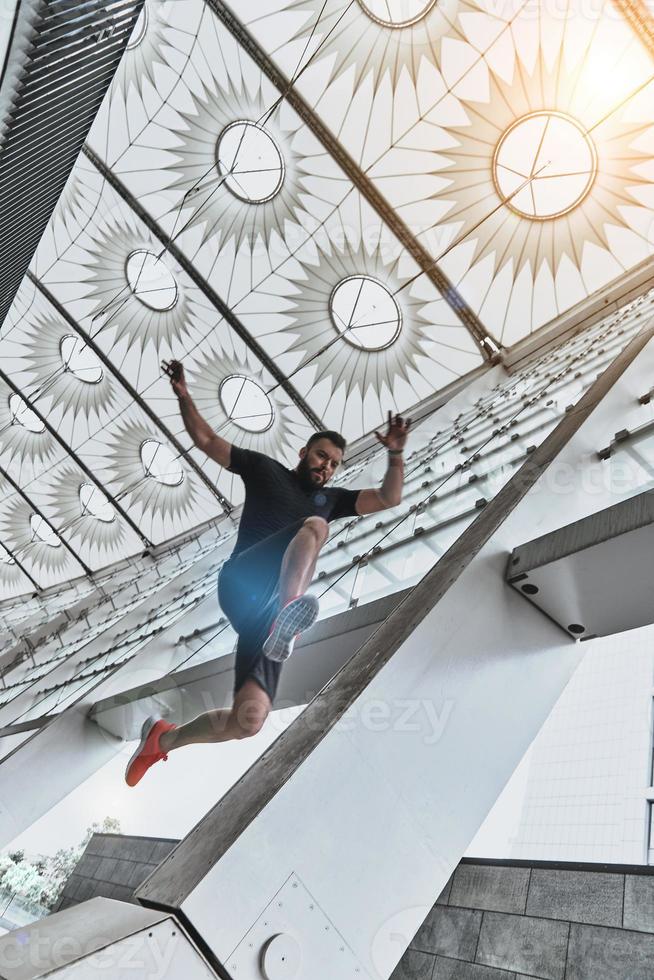 Long jump in the mid-air. Full length of handsome young man in sport clothing jumping while exercising outside photo