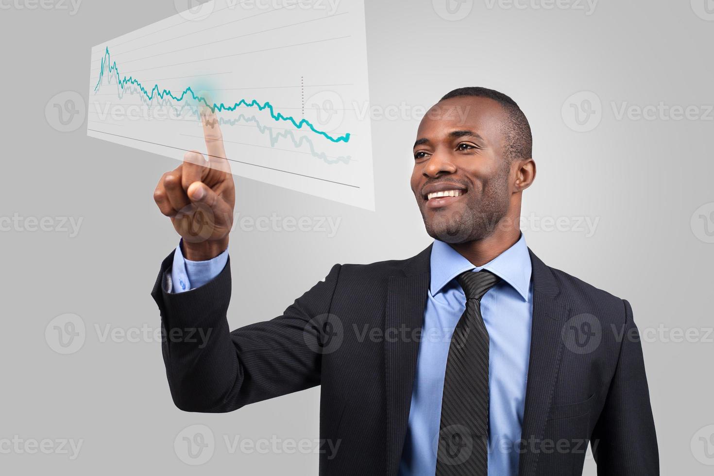 Innovative business. Cheerful young African man in formalwear pointing diagram on the transparent wipe board while standing against grey background photo