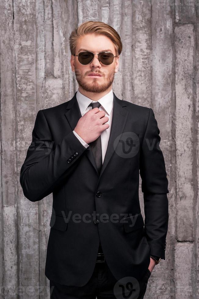 Always in style. Handsome young man in formalwear adjusting his necktie and holding one hand in pocket photo