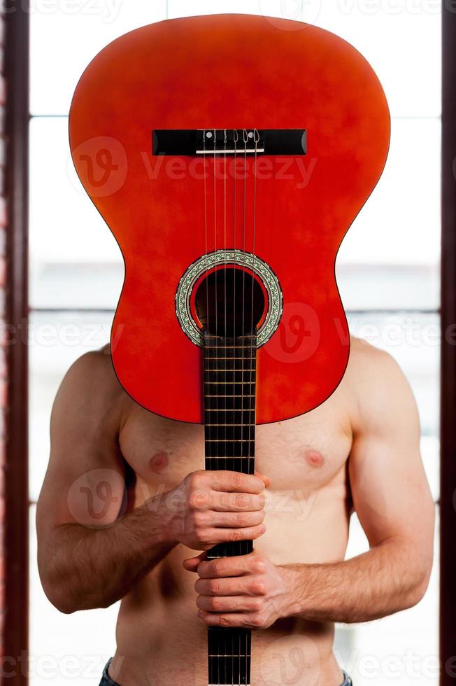 Guitar head. Close-up of man playing acoustic guitar while standing in front of the window photo