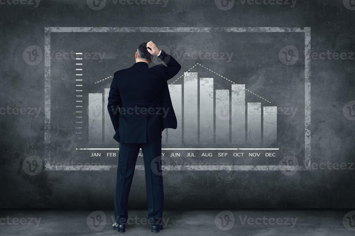 Hard decisions every day. Rear view of mature businessman scratching his head while standing against grey background with illustration of chart photo