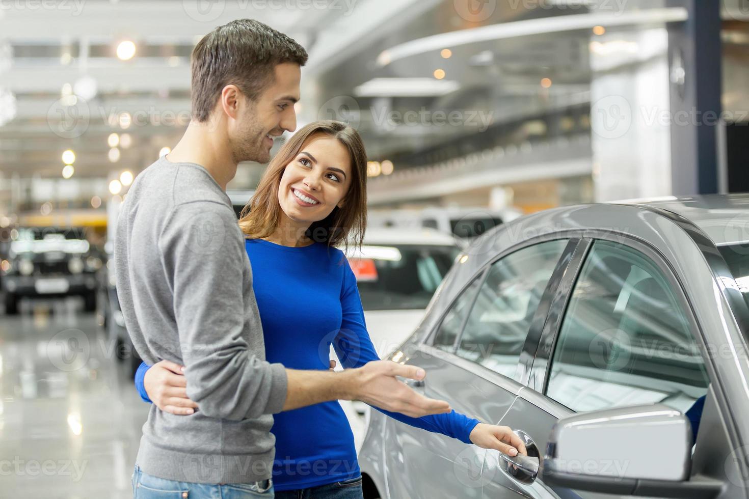 I like this car. Beautiful young couple standing at the dealership choosing the car to buy photo