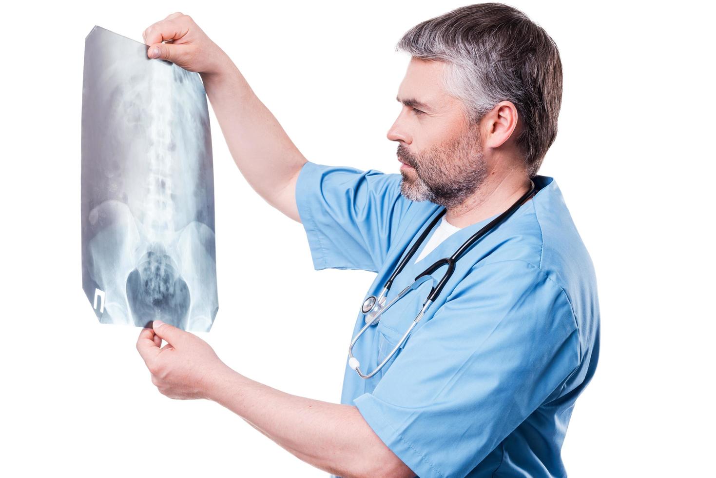 revisando la radiografía. un médico de pelo gris maduro y pensativo que examina la imagen de rayos X mientras está de pie aislado en blanco foto