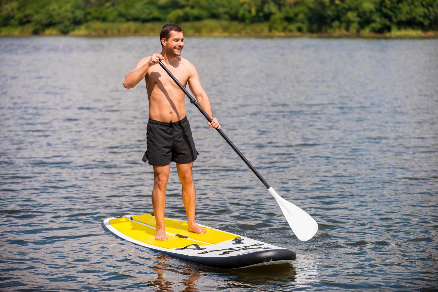 Relaxing on paddleboard. Handsome young man surfing on his paddleboard and smiling photo