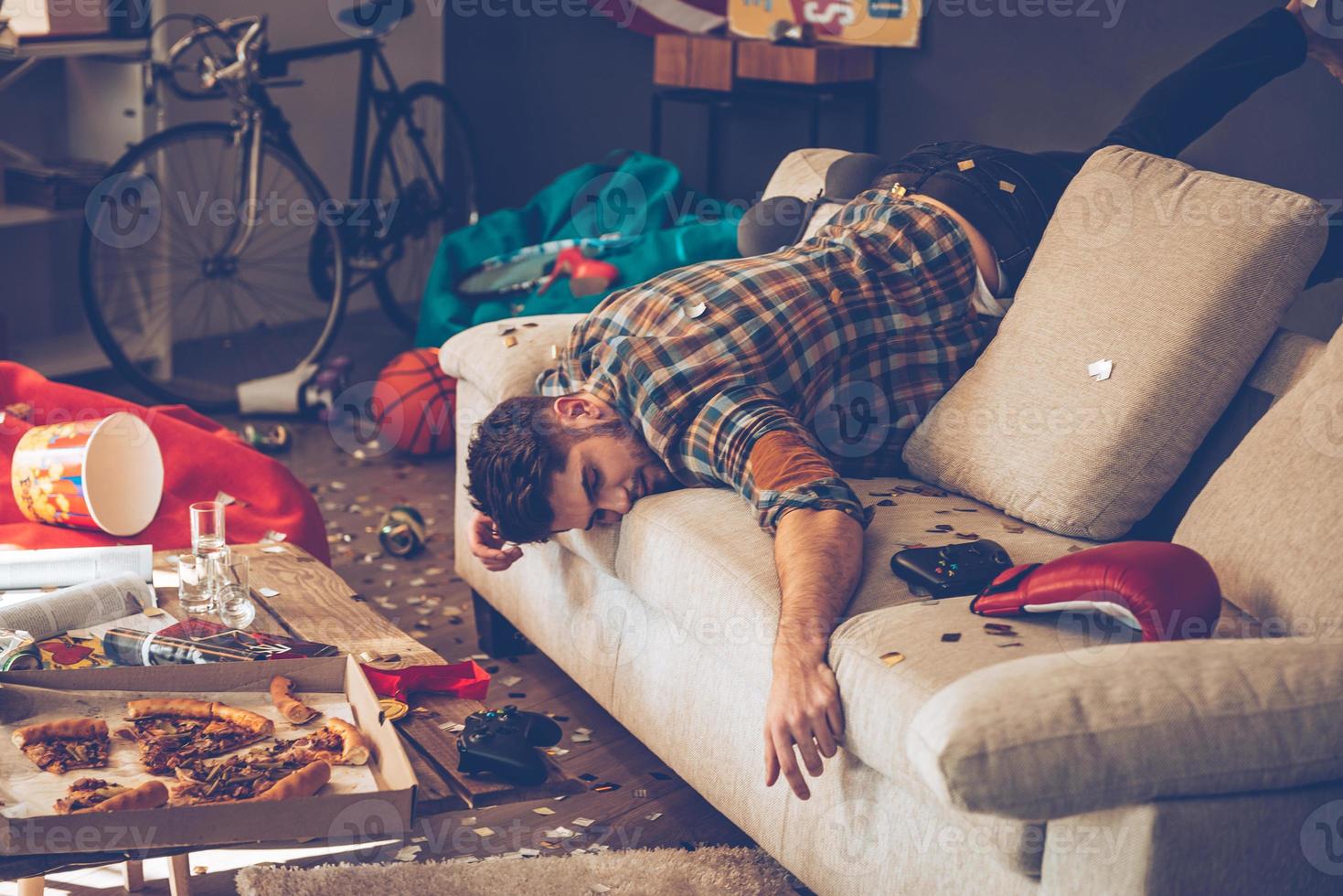 When the party is over. Young handsome man passed out on sofa in messy room after party photo