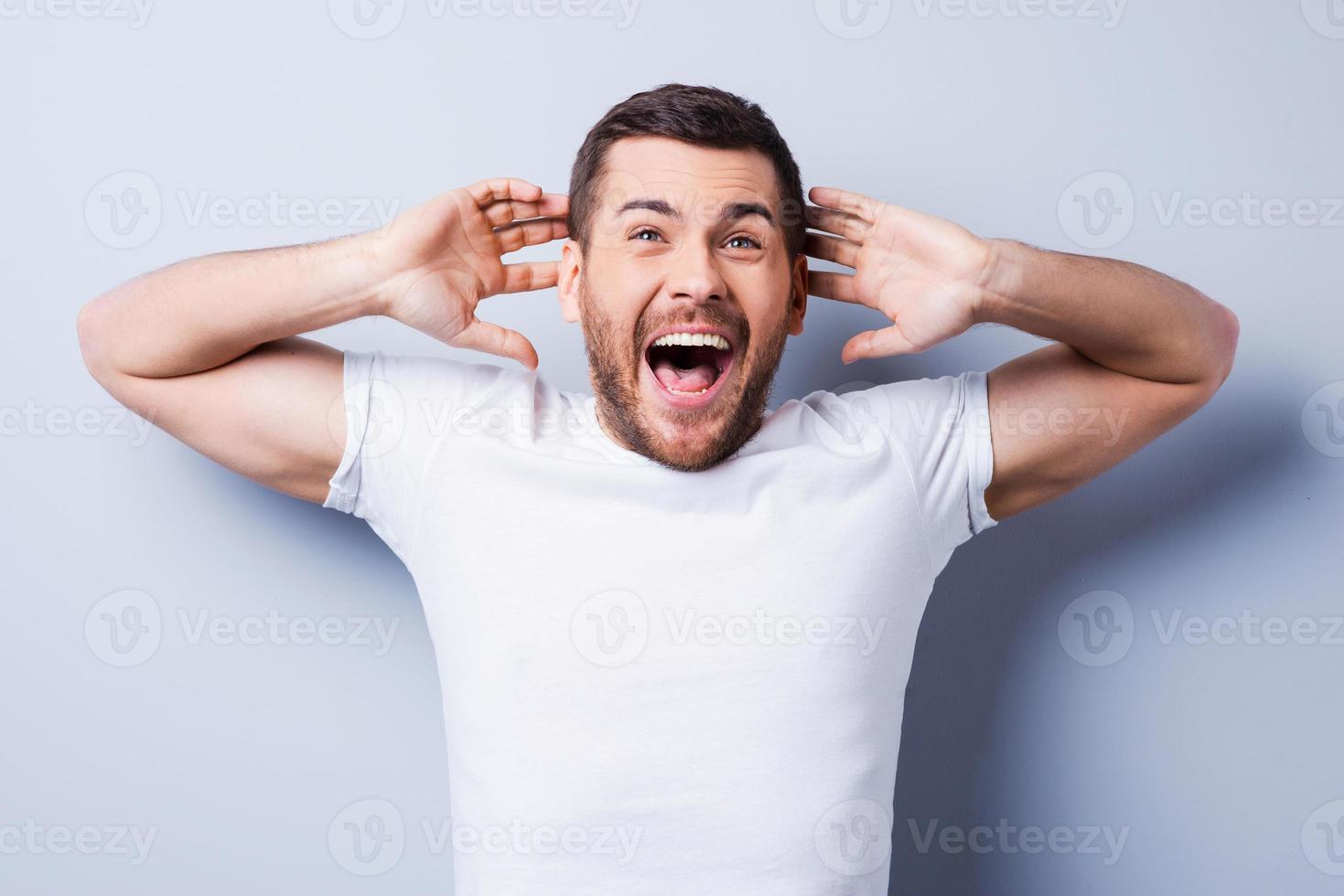 noticias impactantes. sorprendido joven expresando positividad y gesticulando mientras está de pie contra el fondo gris foto