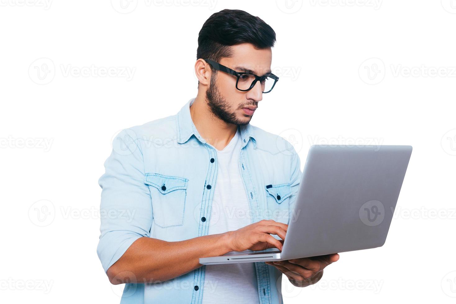 IT professional at work. Confident young Indian man working on laptop while standing against white background photo