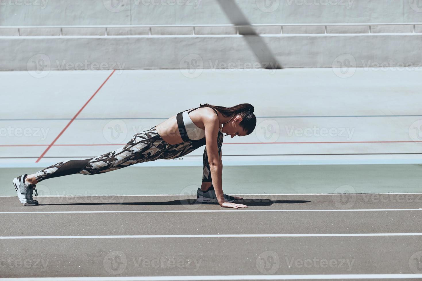 haciendo su mejor esfuerzo. bella joven con ropa deportiva haciendo ejercicio mientras se estira en la pista de atletismo al aire libre foto